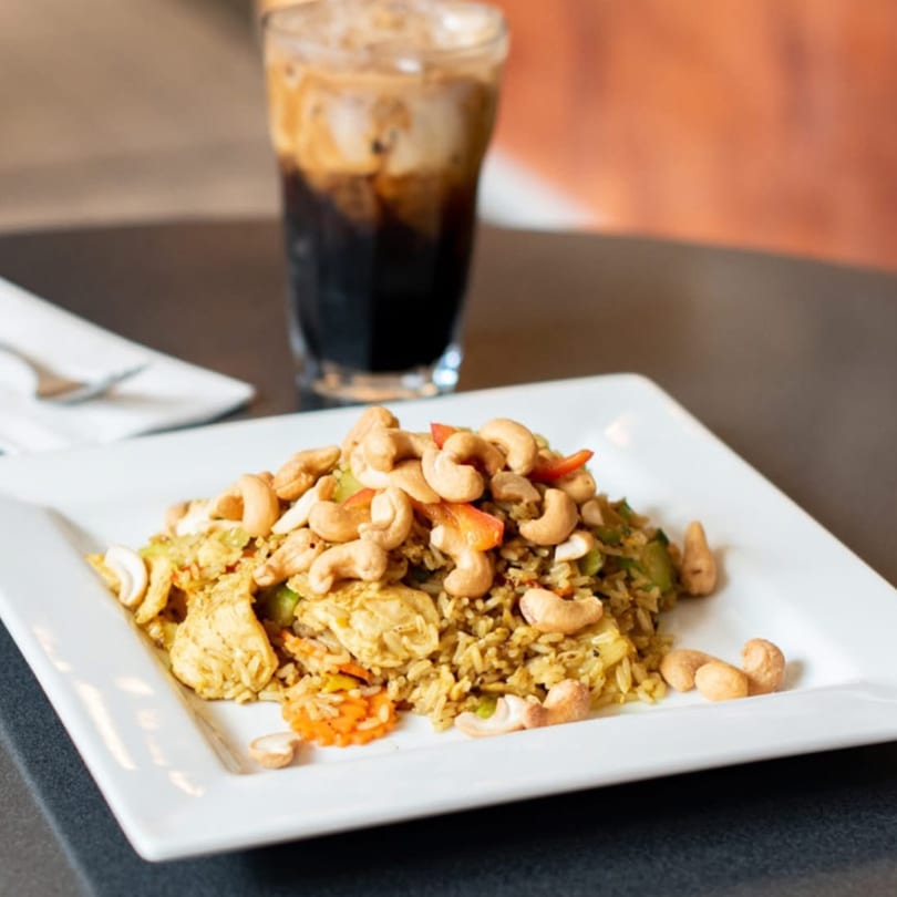 Cashew nut chicken with rice and vegetables, served on a white plate with an iced drink.