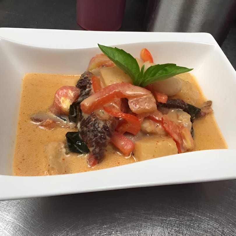 Tuppee Tong Thai red curry with shrimp, red peppers, and basil in a white bowl.