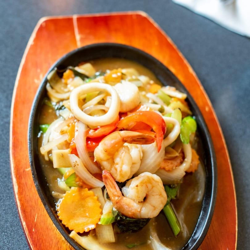 Sizzling Thai seafood dish with shrimp, squid, and vegetables in a rich sauce on a wooden platter.