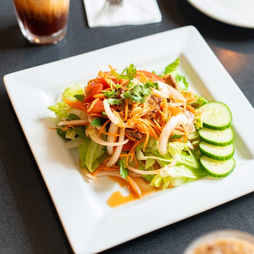 A vibrant Thai salad with lettuce, carrots, onions, tomatoes, and cucumbers on a white plate.